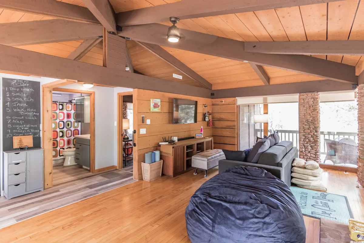 The image features a large bean bag chair, a comfortable sofa, colorful wall art, exposed wooden beams, and abundant natural light streaming in through the windows. The setup is ideal for relaxing with a book or hosting friends, with design details that feel intimate yet open.