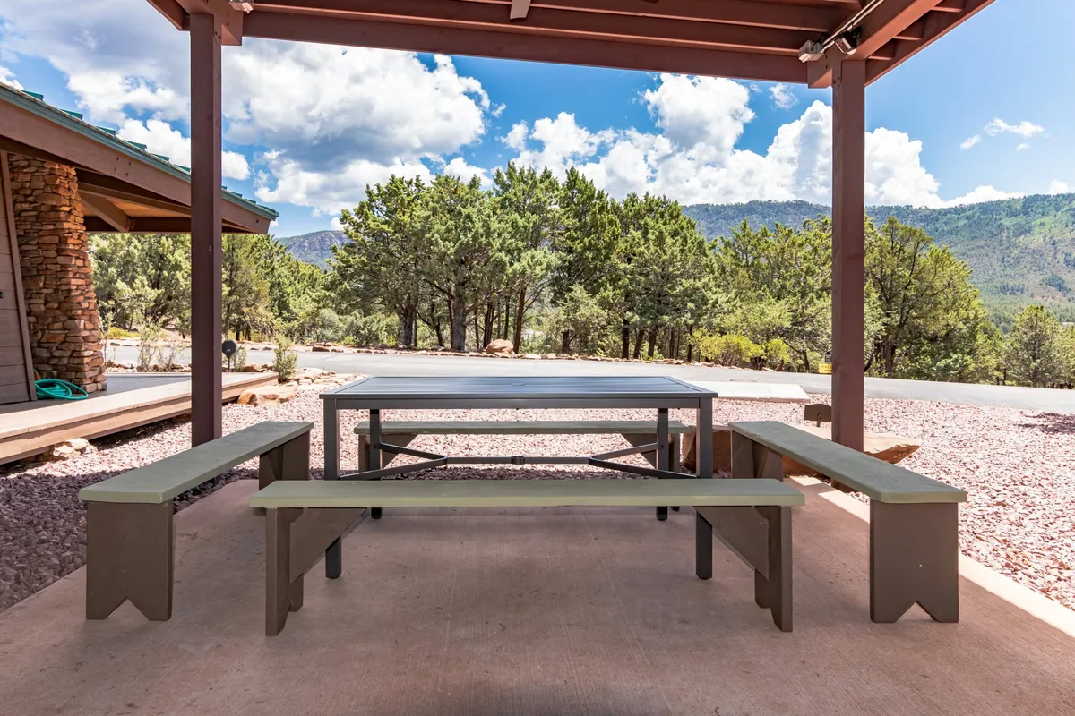 An exterior dining table set on a deck with benches, overlooking a stunning mountain view. The space is designed for outdoor gatherings, inviting guests to enjoy meals al fresco amidst natural beauty.