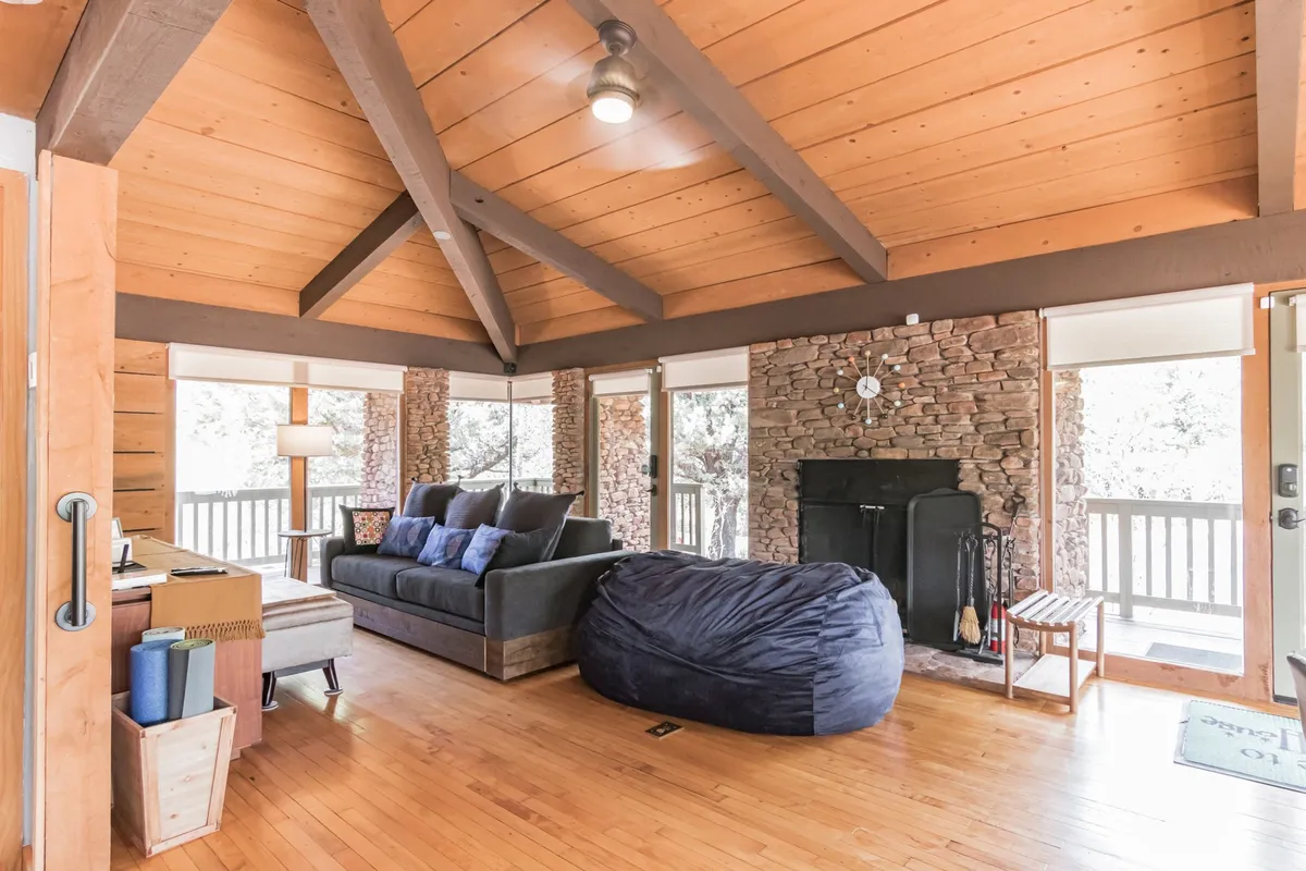 A spacious interior shot with a stone fireplace, comfortable sofa, bean bag chair, and large windows that frame the stunning views outside. The natural light and cozy layout invite relaxation and socializing.