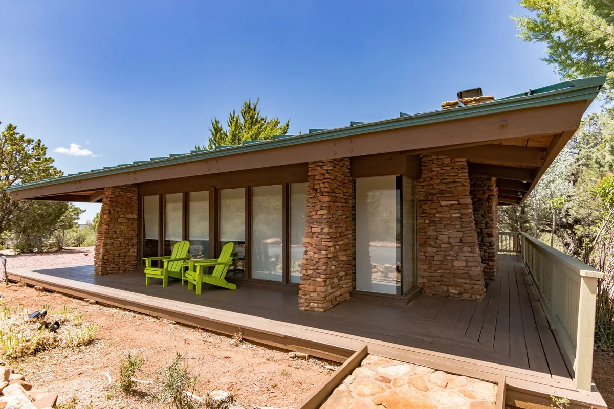 This image captures green Adirondack chairs arranged on a patio or deck, framed by large windows and stone pillars. The setting is tranquil and invites relaxation, with the chairs positioned to enjoy the surrounding views, sunlight, and evening stargazing.