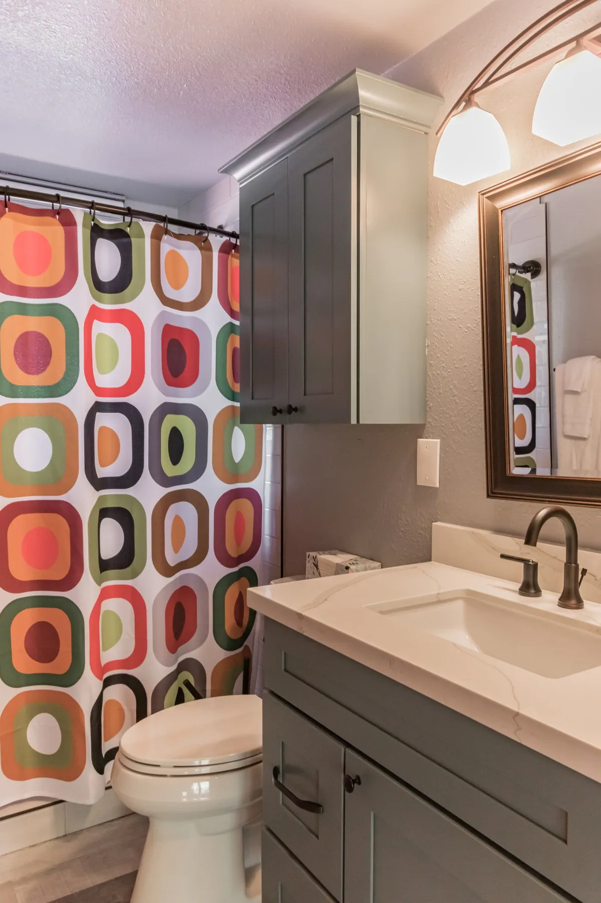 A modern bathroom with a colorful shower curtain, sleek vanity, and a framed mirror. The space is cheerful and inviting, with visible fresh towels and toiletries that enhance the sense of hospitality and care for guests.