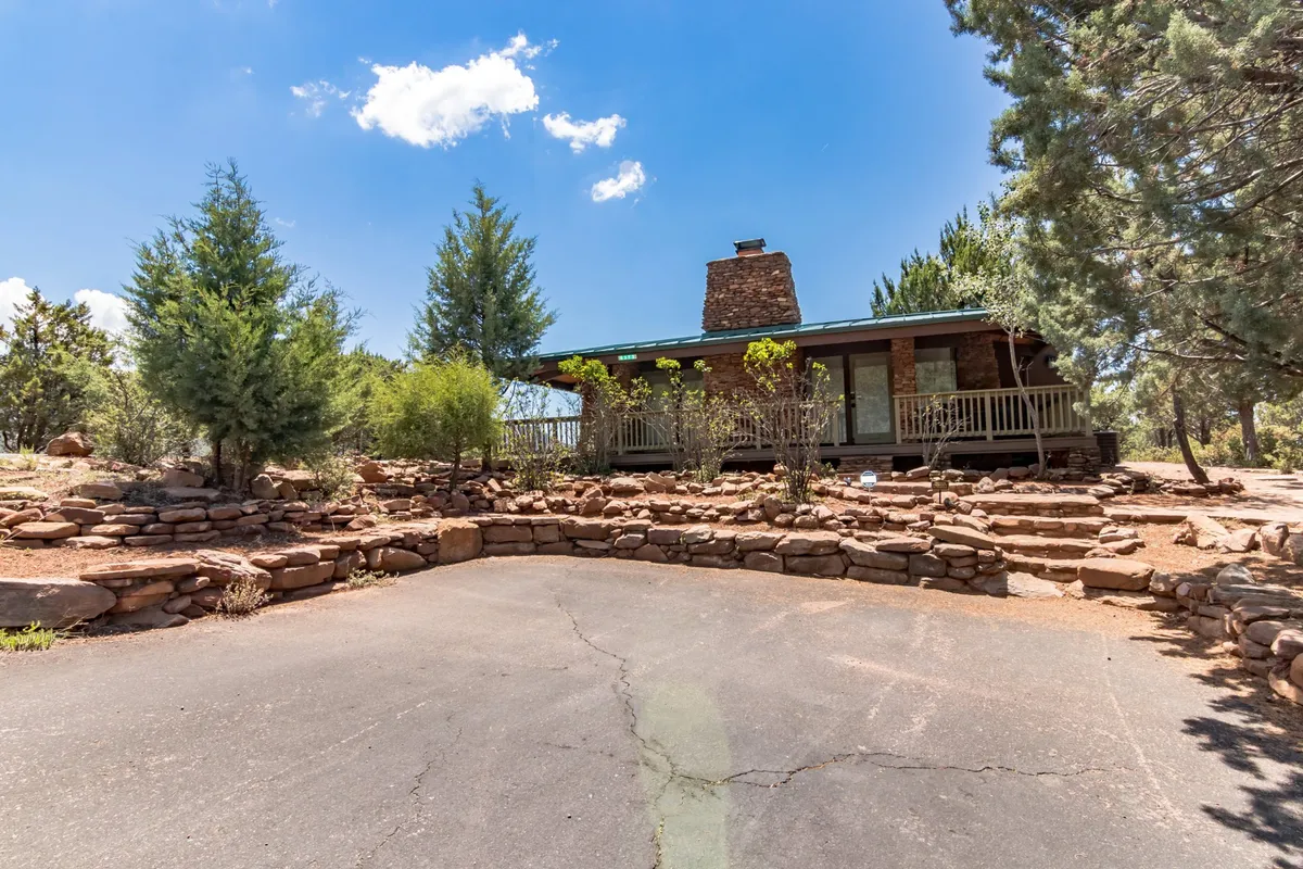 The front porch of the Glass House is featured, framed by a stone chimney, rock landscaping, and towering trees. The porch provides a tranquil environment, ideal for savoring morning coffee, meditating, or journaling while immersed in the calming sounds of nature.