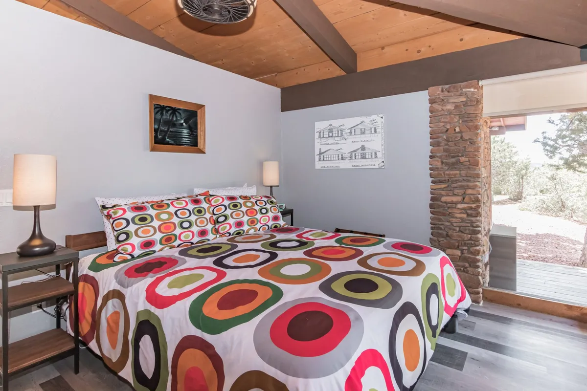 A cozy bedroom spotlighting a king-sized bed with colorful bedding, a rustic stone wall, and unique wall art. The nightstand with a lamp adds a touch of homely comfort, making it ideal for reading or winding down after a day of adventure.