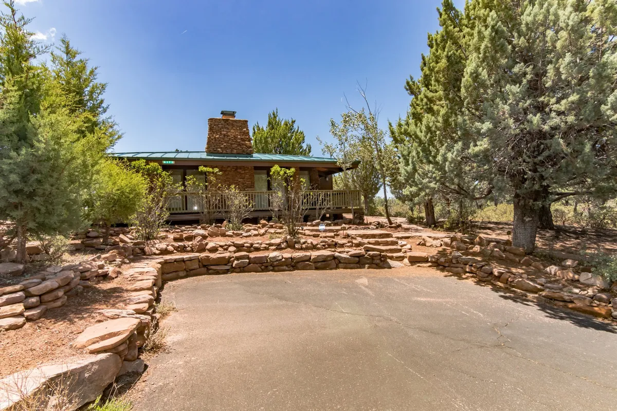 The front porch is surrounded by lush rock landscaping and mature trees, providing a peaceful, natural setting that connects the home to its wild surroundings. The angle from the porch suggests a vantage point for enjoying the outdoors, whether it's watching elk and deer pass by or simply basking in the quiet beauty of the environment.